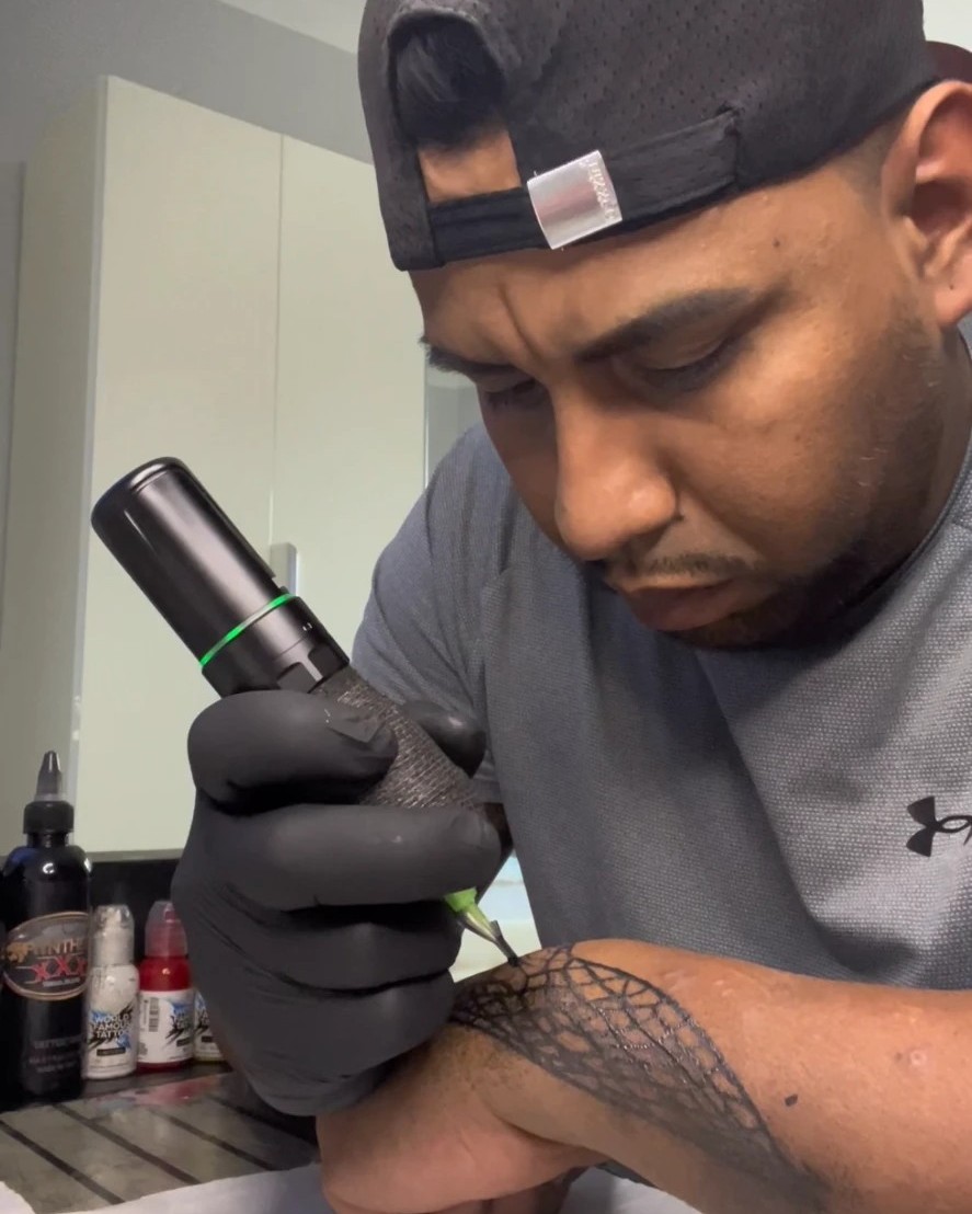 David Enrique Ortega Batista tatuando un antebrazo con una máquina pen inalámbrica, con guantes y piel preparada